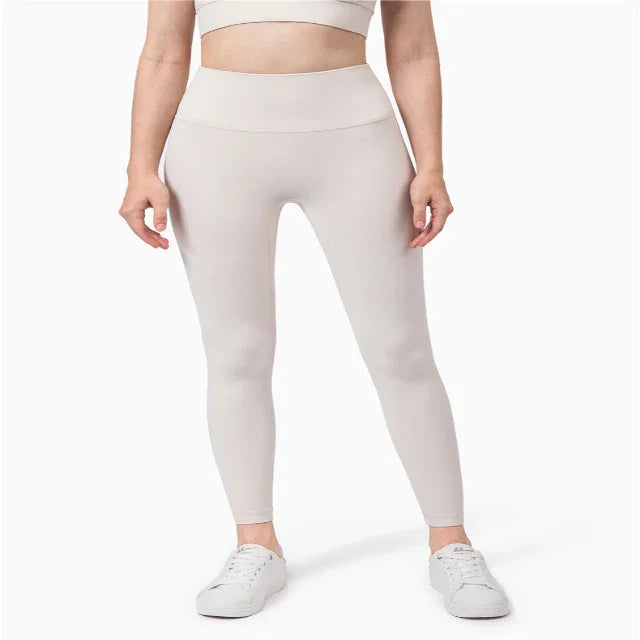 Woman wearing light beige high-waisted leggings and white sneakers, cropped at midriff, on white background