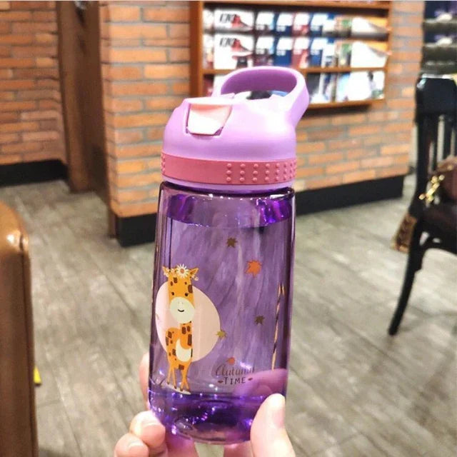 Purple kids water bottle with pink lid and giraffe design, held indoors on wooden floor background