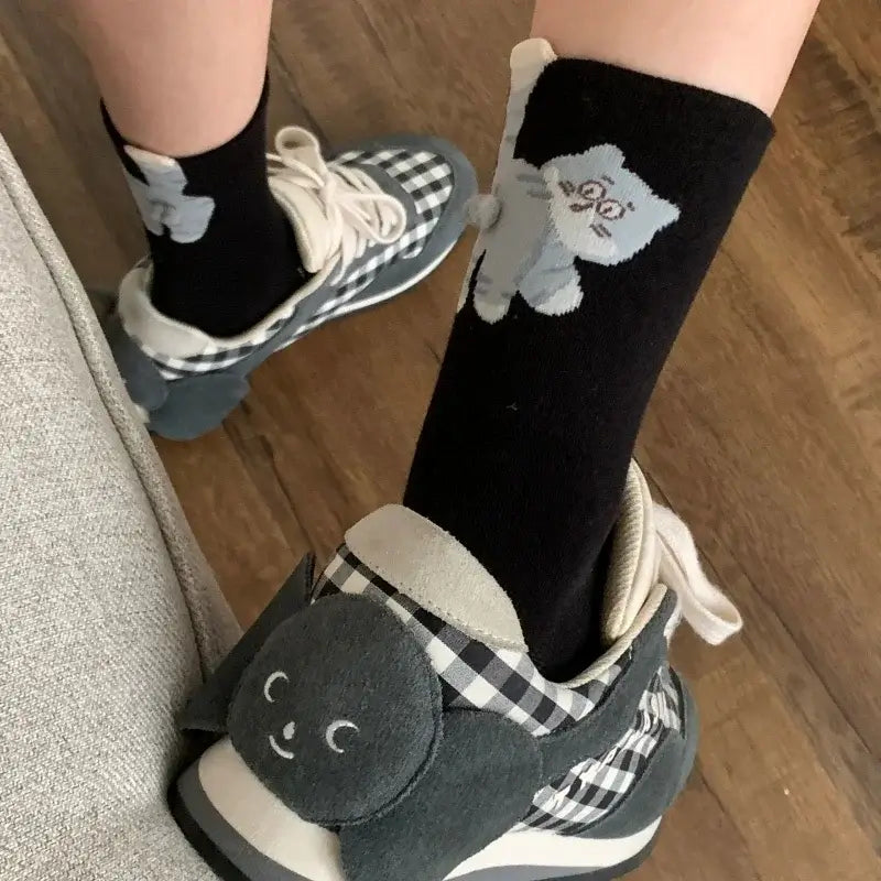 Person wearing black cat socks and checkered sneakers with a playful animal face accent
