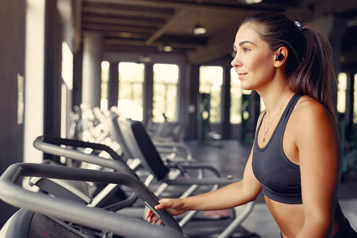 Woman running on treadmill in modern gym, wearing wireless earbuds, fitness equipment visible