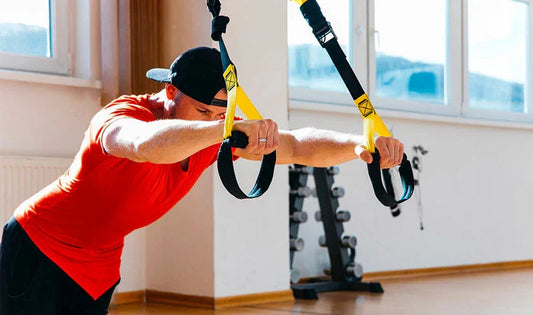 Man using suspension trainer straps in a bright gym for strength training workout