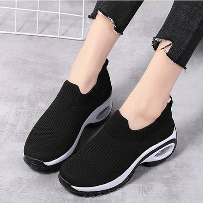 Black slip-on sneakers with white soles worn by a person on a gray background