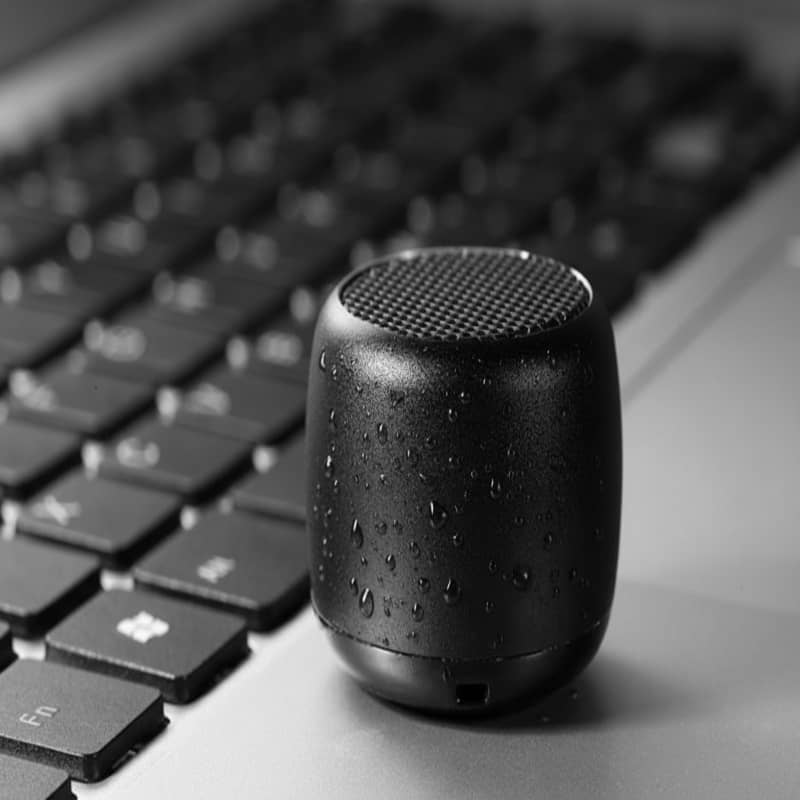 Black portable speaker on a laptop keyboard with water droplets