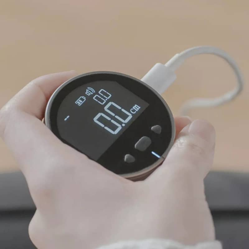 Hand holding a digital device with a screen displaying numbers, against a neutral background