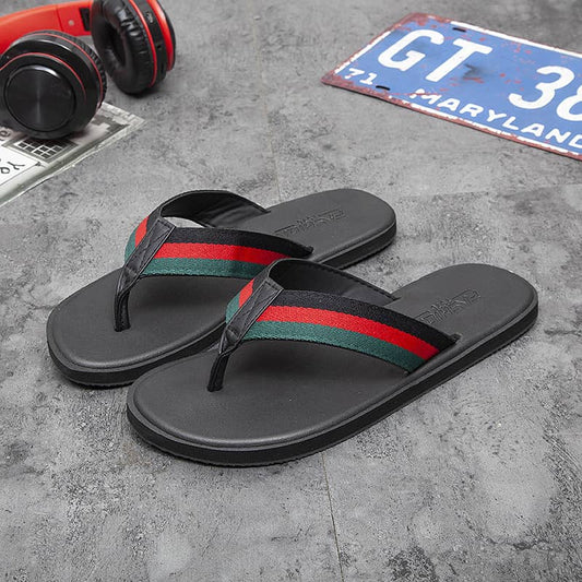 Black flip-flops with red and green stripes on a concrete surface with headphones and a license plate in the background.