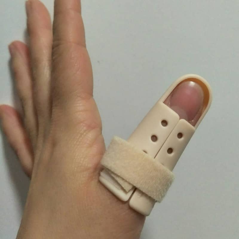 Hand wearing a beige finger splint on a plain background