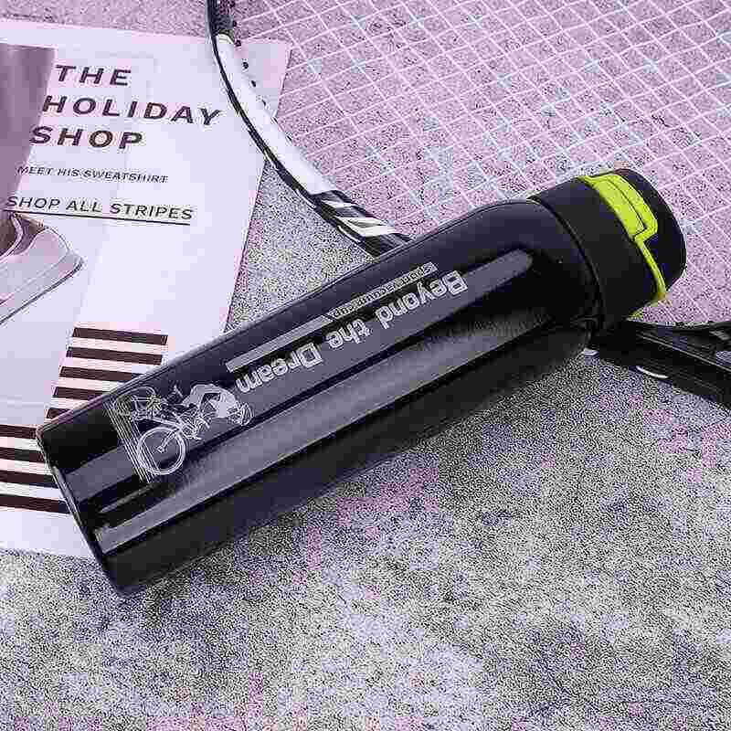 Black sports water bottle with cycling graphic, badminton racket, and magazine on textured surface