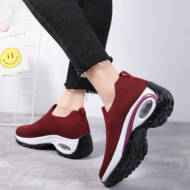 Red slip-on sneakers with white soles worn by a person on a light gray background