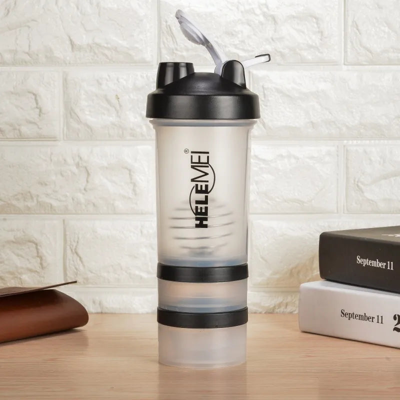 A clear plastic shaker bottle with a black lid and straw, featuring the brand name 'HEFEIMEI' printed vertically on the front. The bottle is set on a wooden surface against a white brick wall background, with books on the right side.