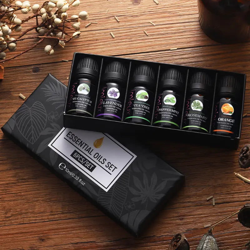 Set of essential oils in a black box on a wooden surface with decorative elements.