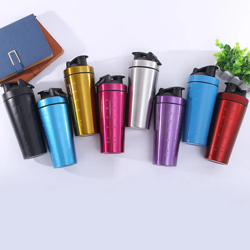 Eight insulated metal shaker cups in assorted colors including black, blue, gold, pink, silver, purple, light blue, and red, arranged in a row on a light background with a notebook and small plant as props.