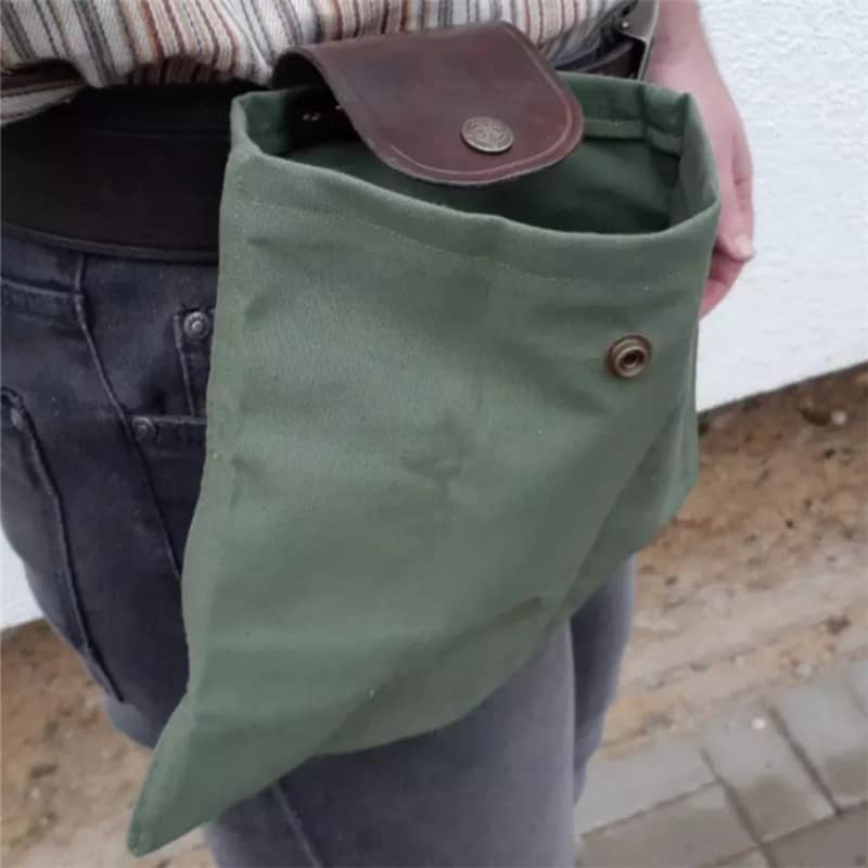 Green fabric pouch with leather flap held by a person outdoors.