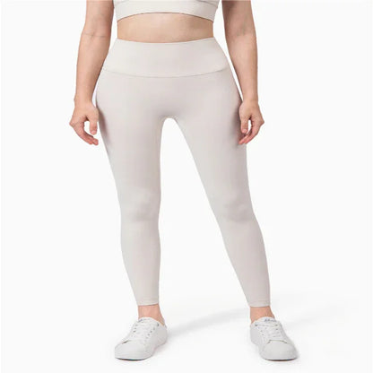 Woman wearing light beige high-waisted leggings and white sneakers, cropped at midriff, on white background