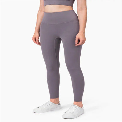 Woman wearing gray high-waisted fitness leggings and white sneakers on white background
