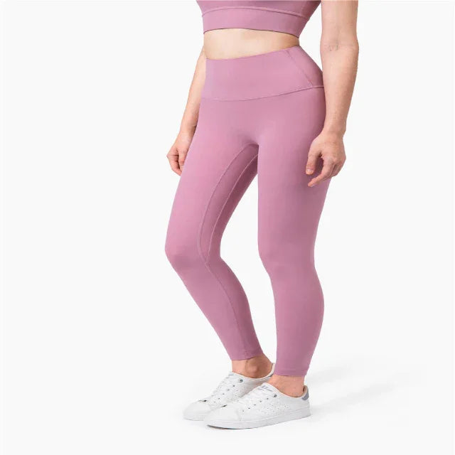 Woman wearing mauve high-waisted leggings and matching sports bra with white sneakers on white background