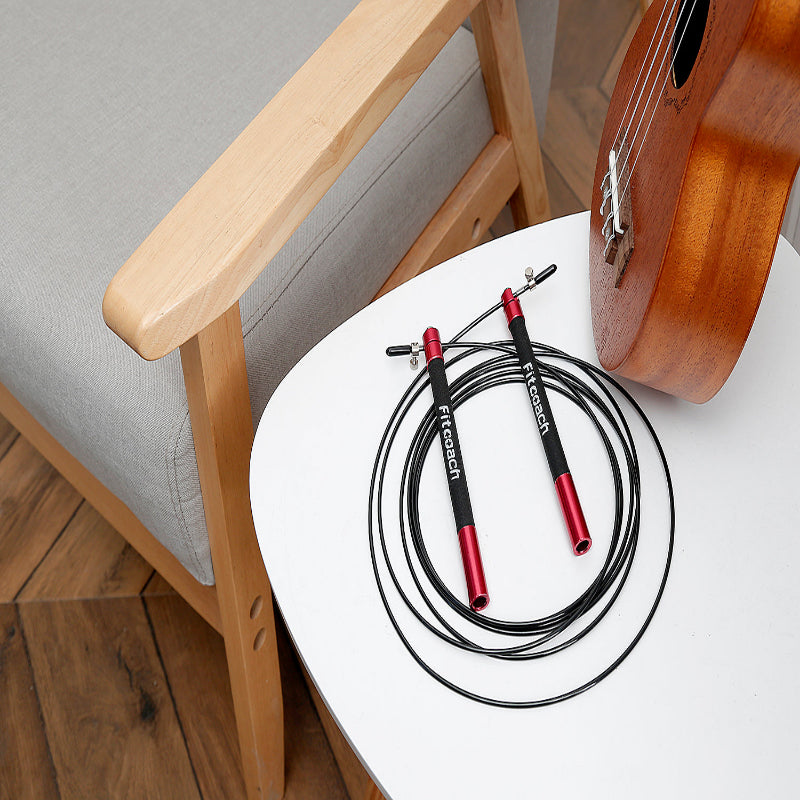 Red and black jump rope on a white table next to a wooden chair and ukulele.