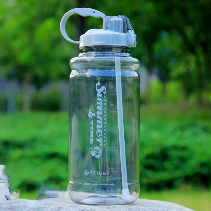 Clear plastic water bottle with straw and summer design on stone outdoors with green blurred background