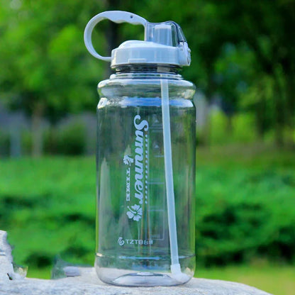 Clear plastic water bottle with straw and summer design on stone outdoors with green blurred background