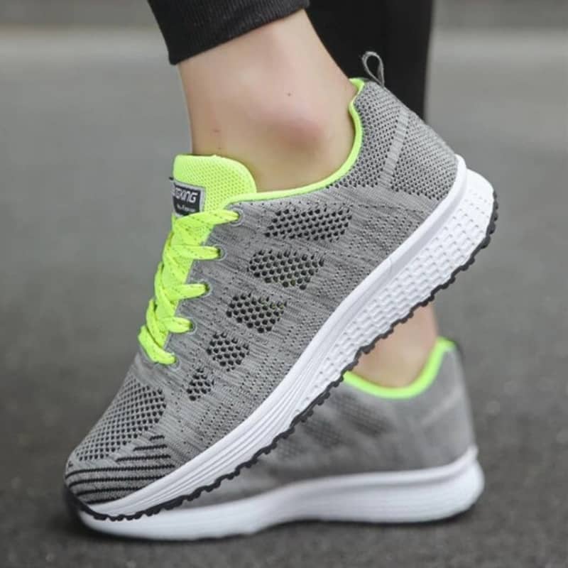 Gray sneakers with neon green accents worn on a blurred background