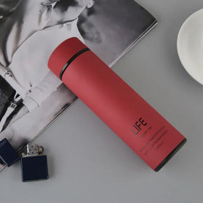 Red stainless steel insulated water bottle on a gray surface next to a silver lighter and a black-and-white magazine