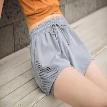A person wearing light blue athletic shorts with a drawstring waist and perforated mesh side panels, paired with an orange top, sitting on a wooden deck.