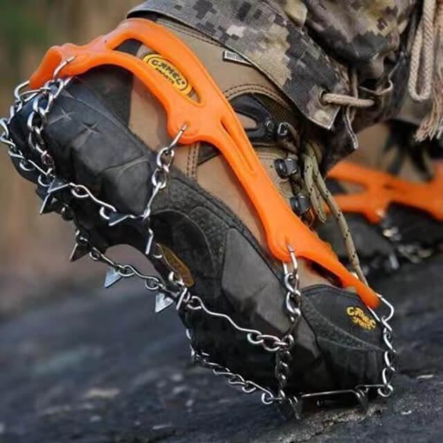 Hiking boot wearing orange ice traction crampons with metal spikes on rocky outdoor terrain