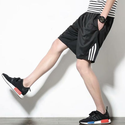Person wearing black shorts with white stripes and black sneakers on a plain background