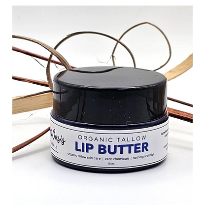 A small jar of organic tallow lip butter with a black lid and white label, photographed on a white background with decorative dried stems behind it.