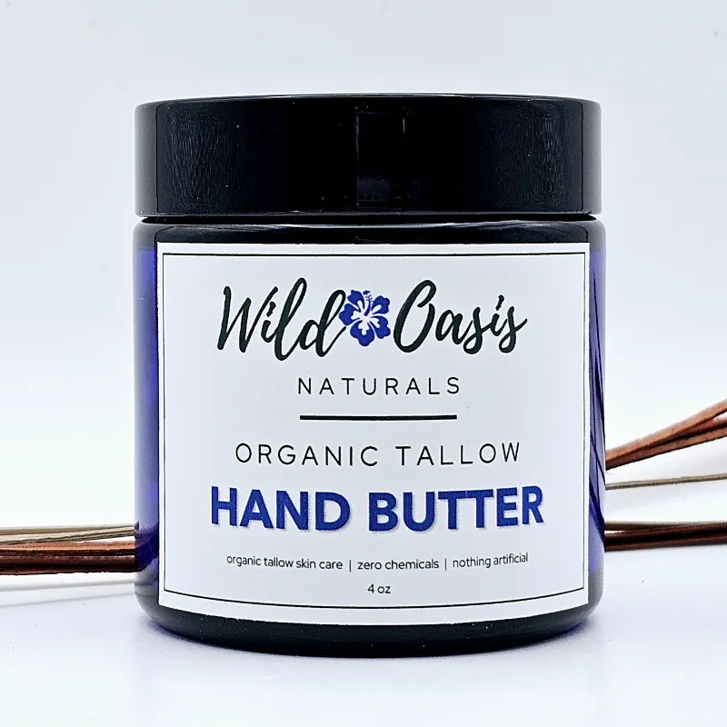 A jar of Wild Oasis Naturals Organic Tallow Hand Butter, featuring a black lid and a white label with blue and black text, set against a clean white background with decorative copper wire elements.