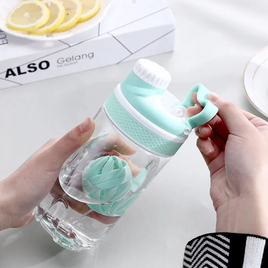 Clear water bottle with a green silicone sleeve held by two hands on a light surface.