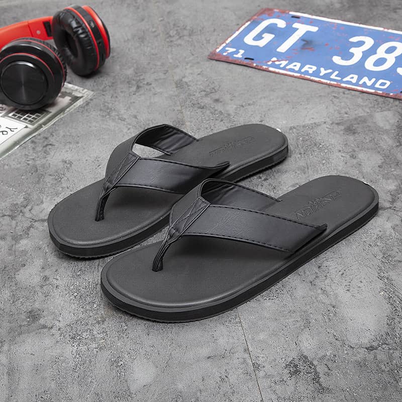 Black flip-flops on a gray surface with headphones and a license plate in the background.