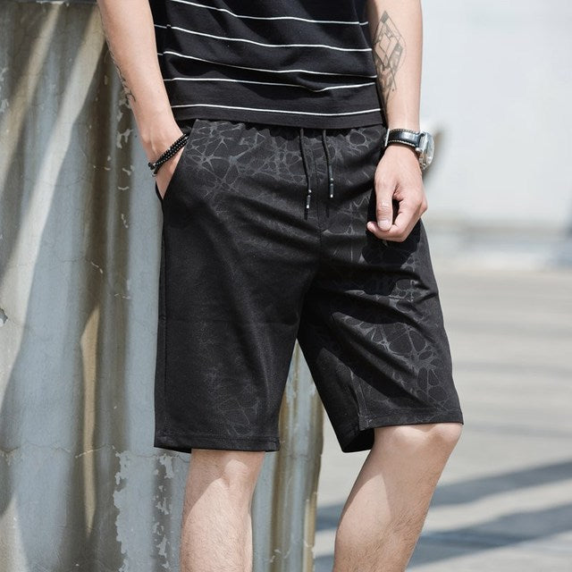 Person wearing black patterned shorts and a striped shirt against a neutral background