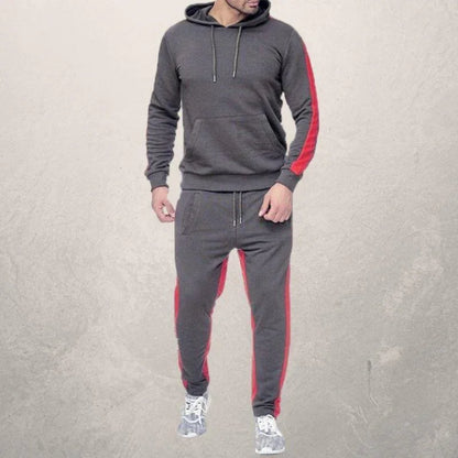 man wearing gray hoodie and joggers with red side stripes, modeling casual fitness outfit
