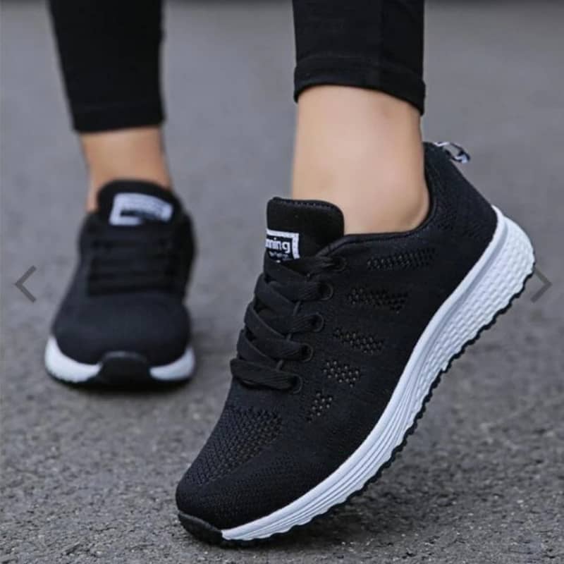 Black running shoes with white soles worn by a person on a gray pavement.