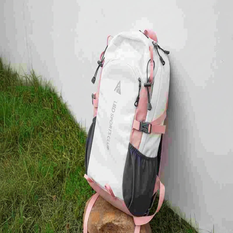 White and pink backpack with black straps on a stone surface against a white wall.