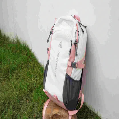 White and pink backpack with black straps on a stone surface against a white wall.