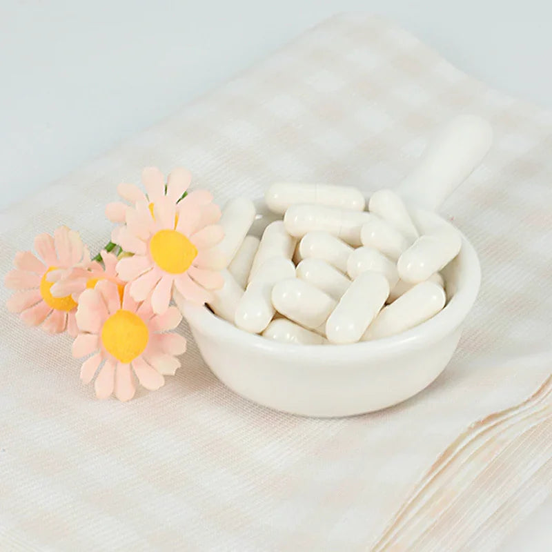 White capsules in a white ceramic scoop with pink and yellow flowers on a light striped cloth