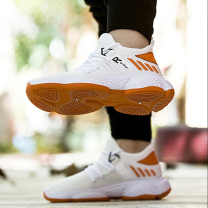 Person wearing white and orange athletic sneakers with textured soles, posing outdoors on wooden floor