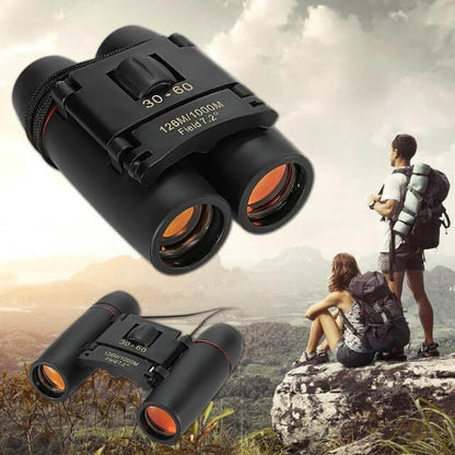Black binoculars with orange lenses on a scenic background of two people with backpacks.