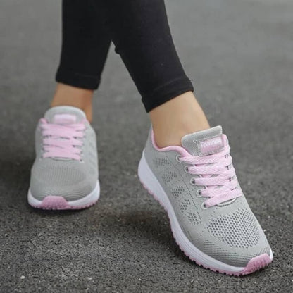 Gray sneakers with pink laces worn on a gray pavement