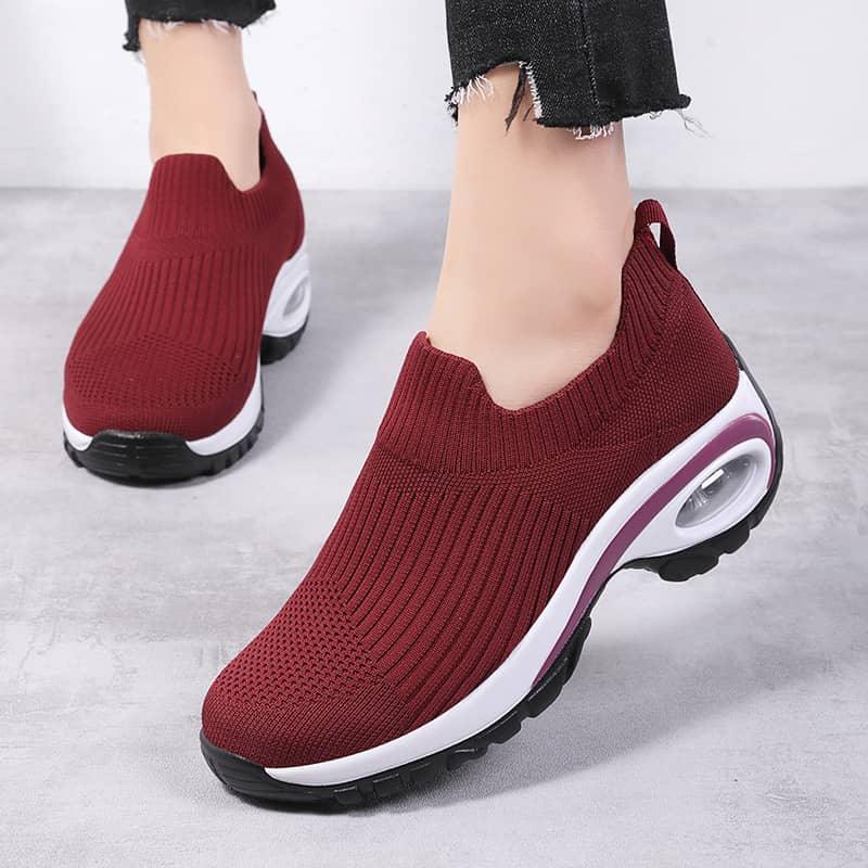 Red slip-on sneakers with white soles worn by a person on a light gray background