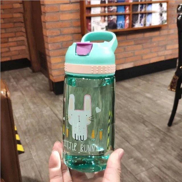 Hand holding a teal water bottle with a pink latch, featuring a cartoon bunny and carrots design, indoor fitness setting