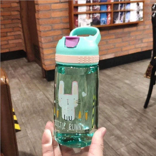 Hand holding a teal water bottle with a pink latch, featuring a cartoon bunny and carrots design, indoor fitness setting