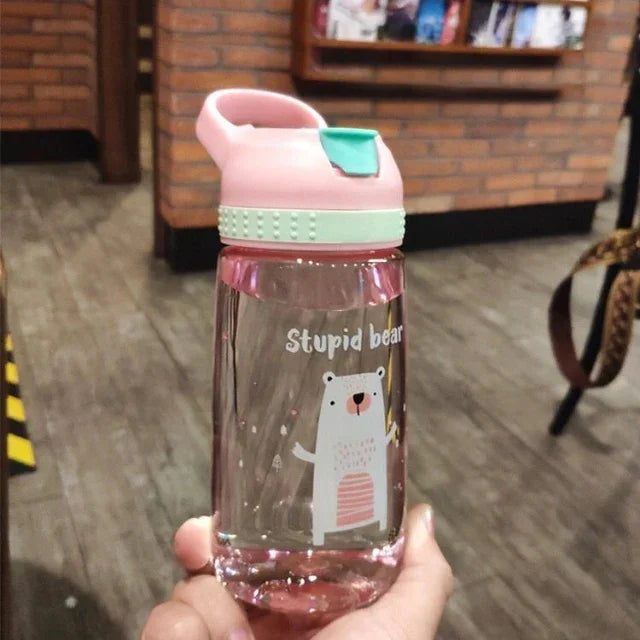Hand holding a clear pink water bottle with a playful polar bear design and pink lid in indoor setting