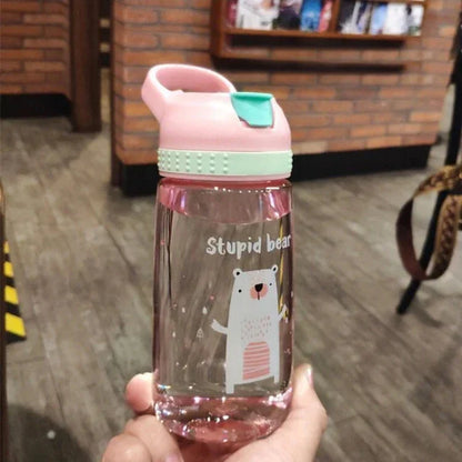 Hand holding a clear pink water bottle with a playful polar bear design and pink lid in indoor setting