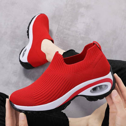 Red slip-on sneakers with white soles held by a person against a gray background