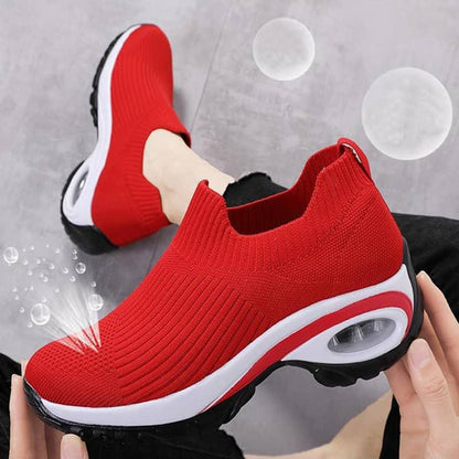 Red slip-on sneakers with white soles held by a hand against a gray background with bubbles.