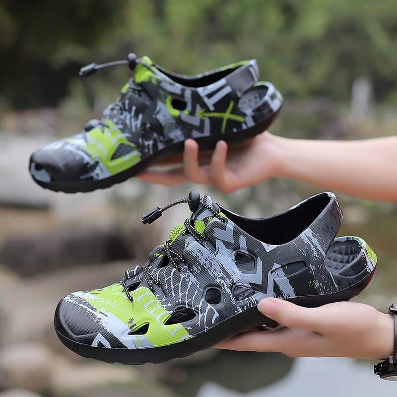 Gray and green water shoes held by a person with a blurred natural background