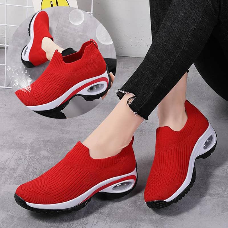 Red slip-on shoes with white soles worn by a person on a gray floor.