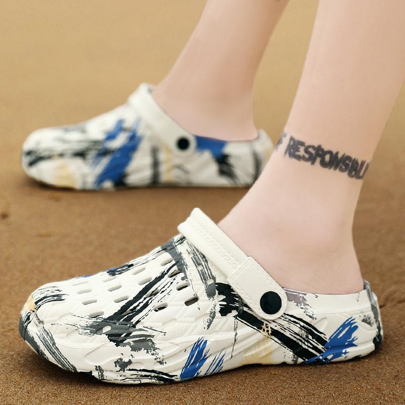 White clogs with black and blue abstract design worn on a sandy surface.
